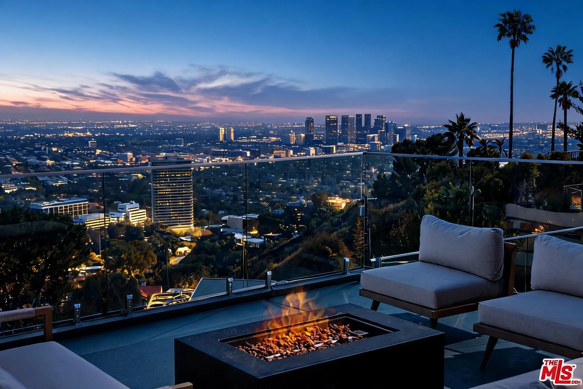 Fire pit lounge with armchairs, glass railing and Century City skyline at dusk
