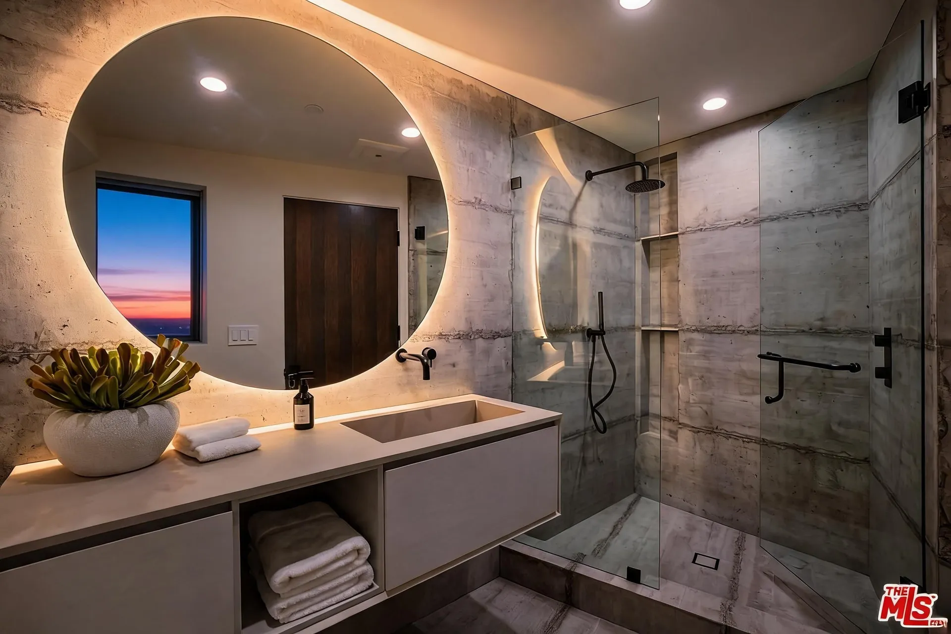 Spa bathroom with stone tile, backlit mirror and glass shower