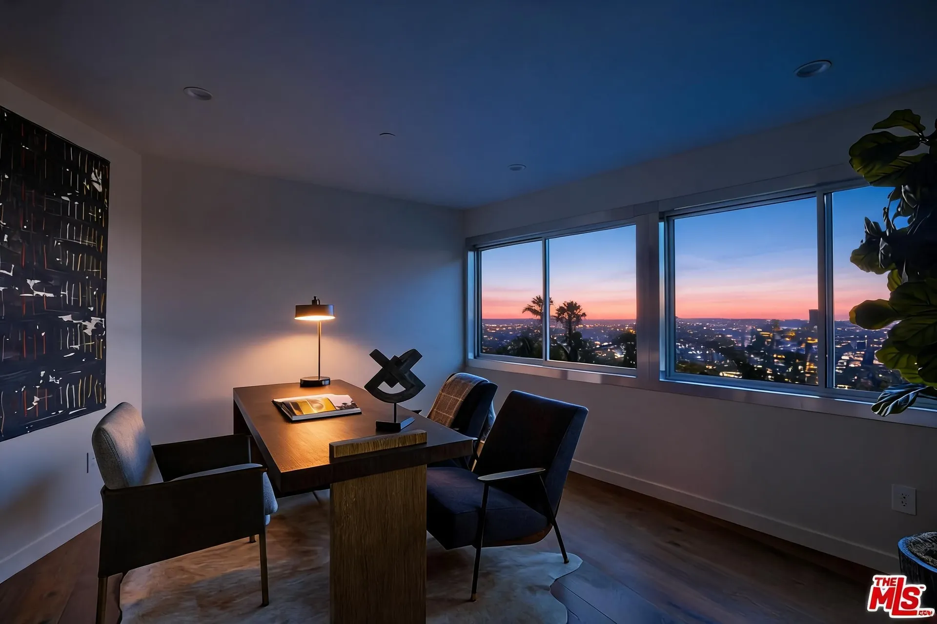 Home study with wood desk, leather chairs and skyline view at dusk